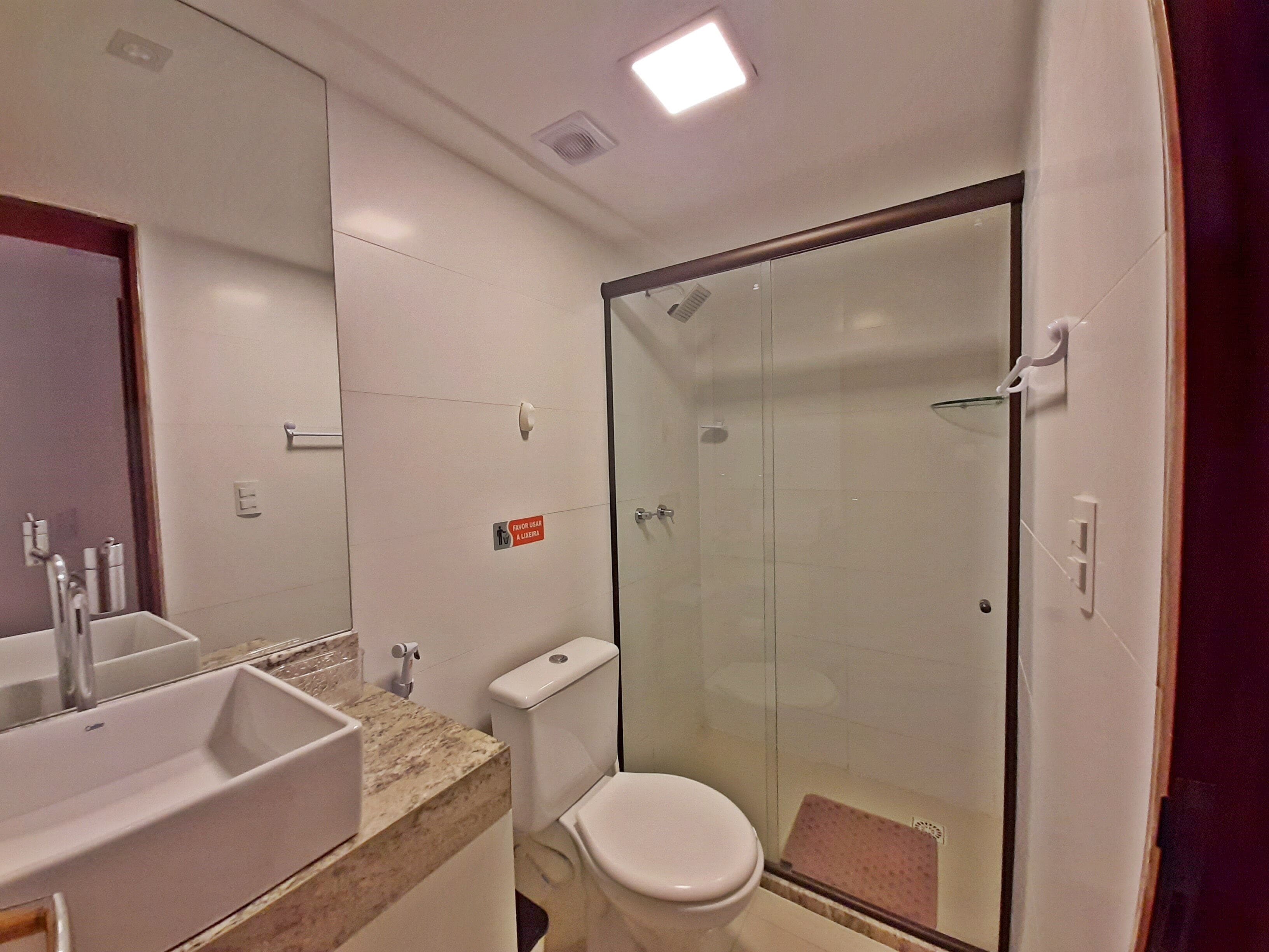 A bathroom with a glass-enclosed shower, a sink with a marble countertop, and a toilet.