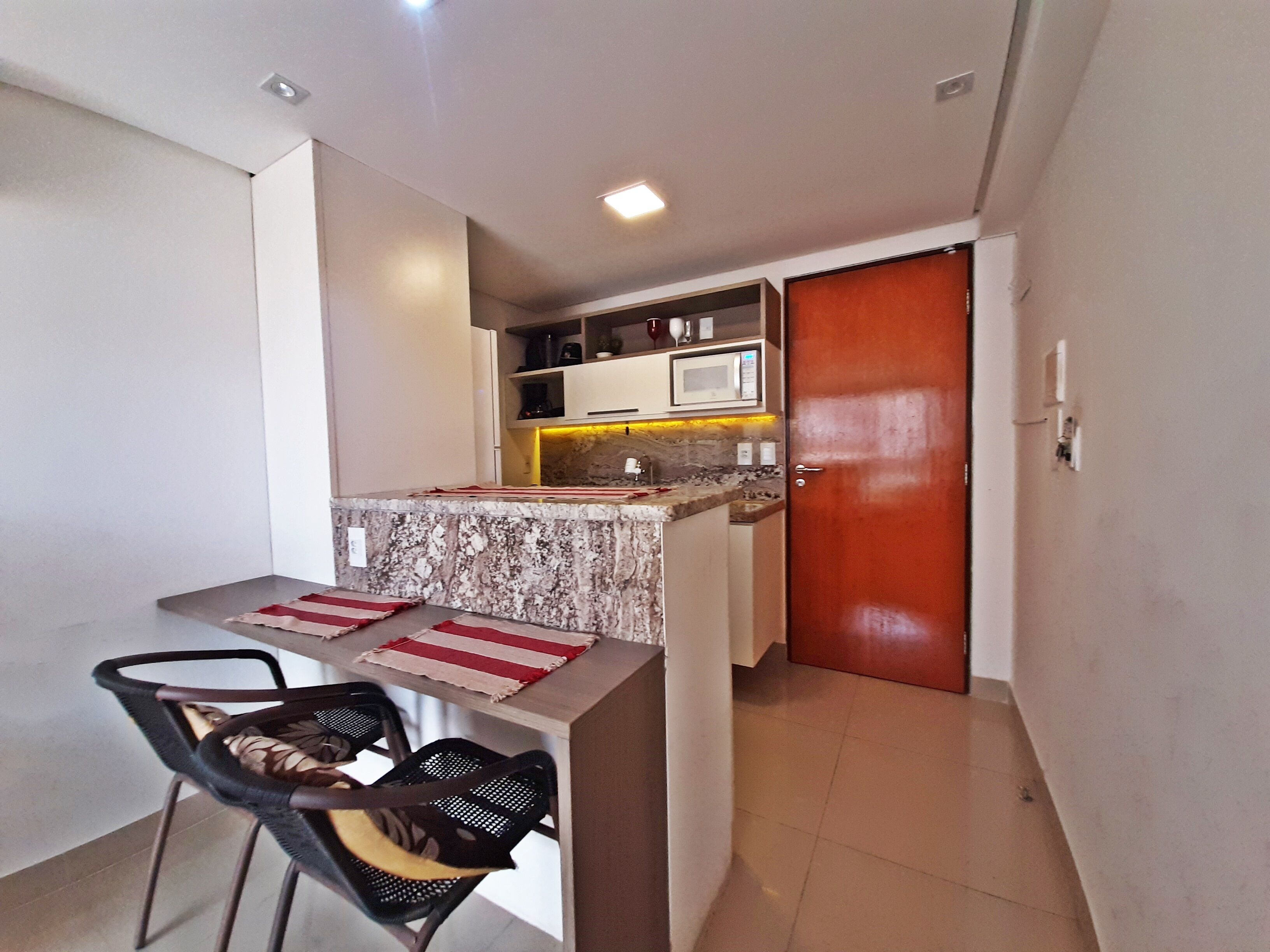 A compact kitchen with a microwave, stove, and cabinets, a dining area with a table and chairs, and a wooden door.