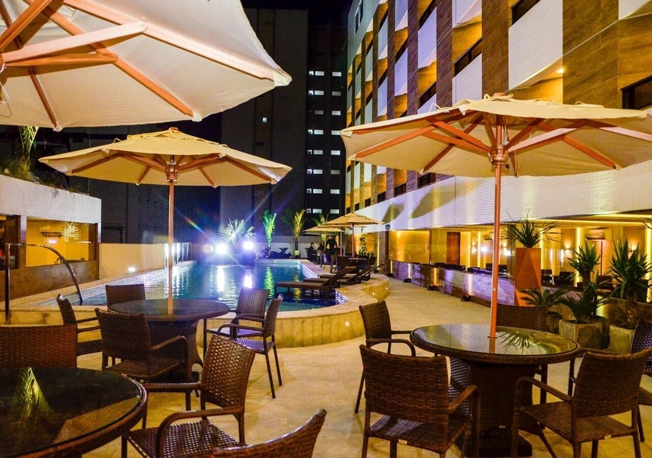 An outdoor pool area with lounge chairs and umbrellas, surrounded by a modern building with multiple floors.