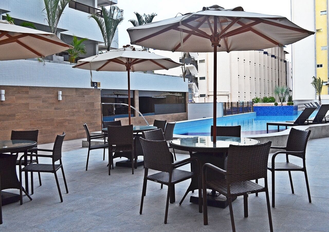 An outdoor pool area with lounge chairs and umbrellas, surrounded by a modern building with a tiled exterior.