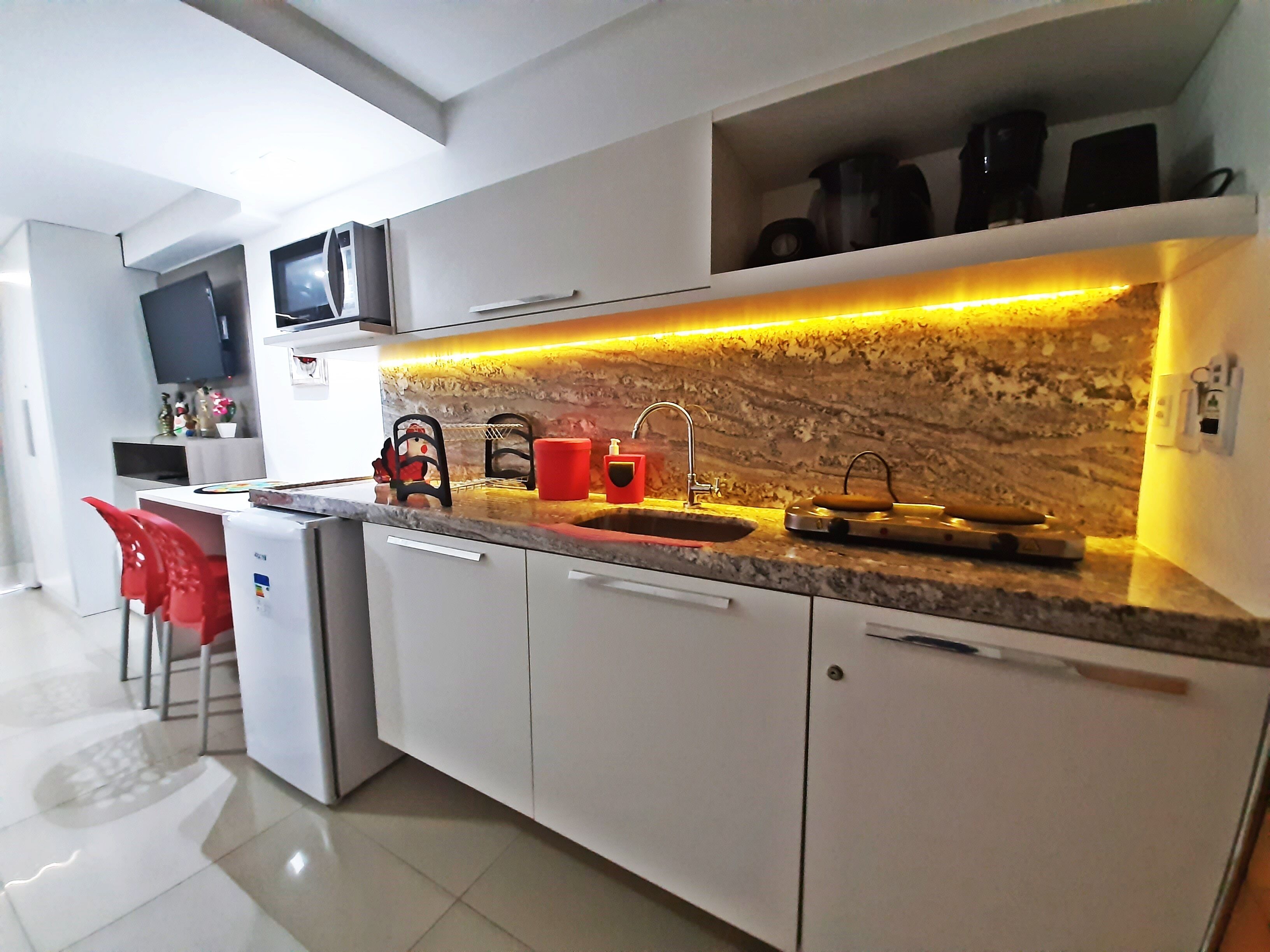 Una cocina moderna con encimera de granito, armarios blancos, microondas integrado y una tetera roja.