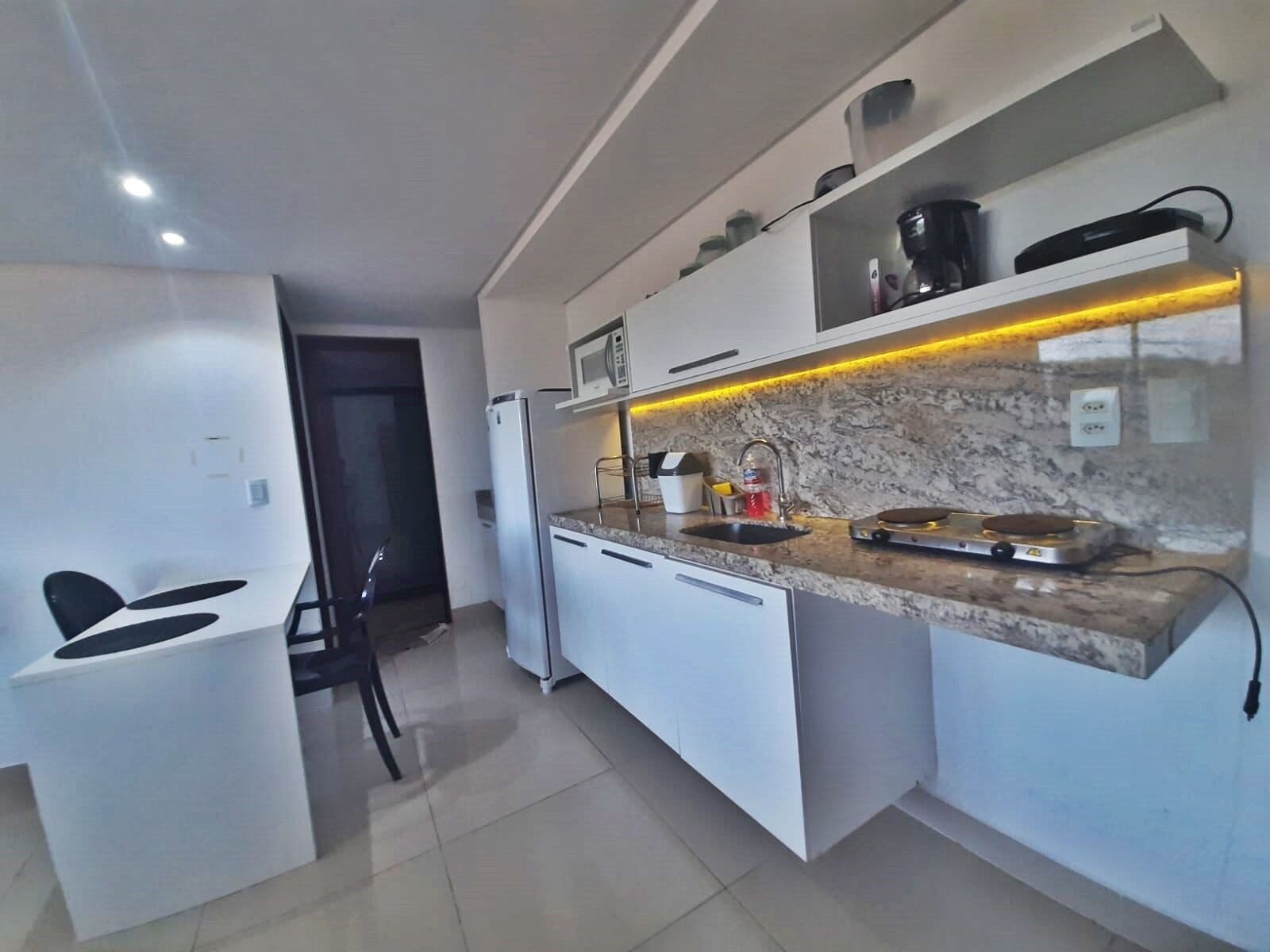 A compact kitchen with white cabinetry, a granite countertop, a built-in microwave, and a coffee maker.