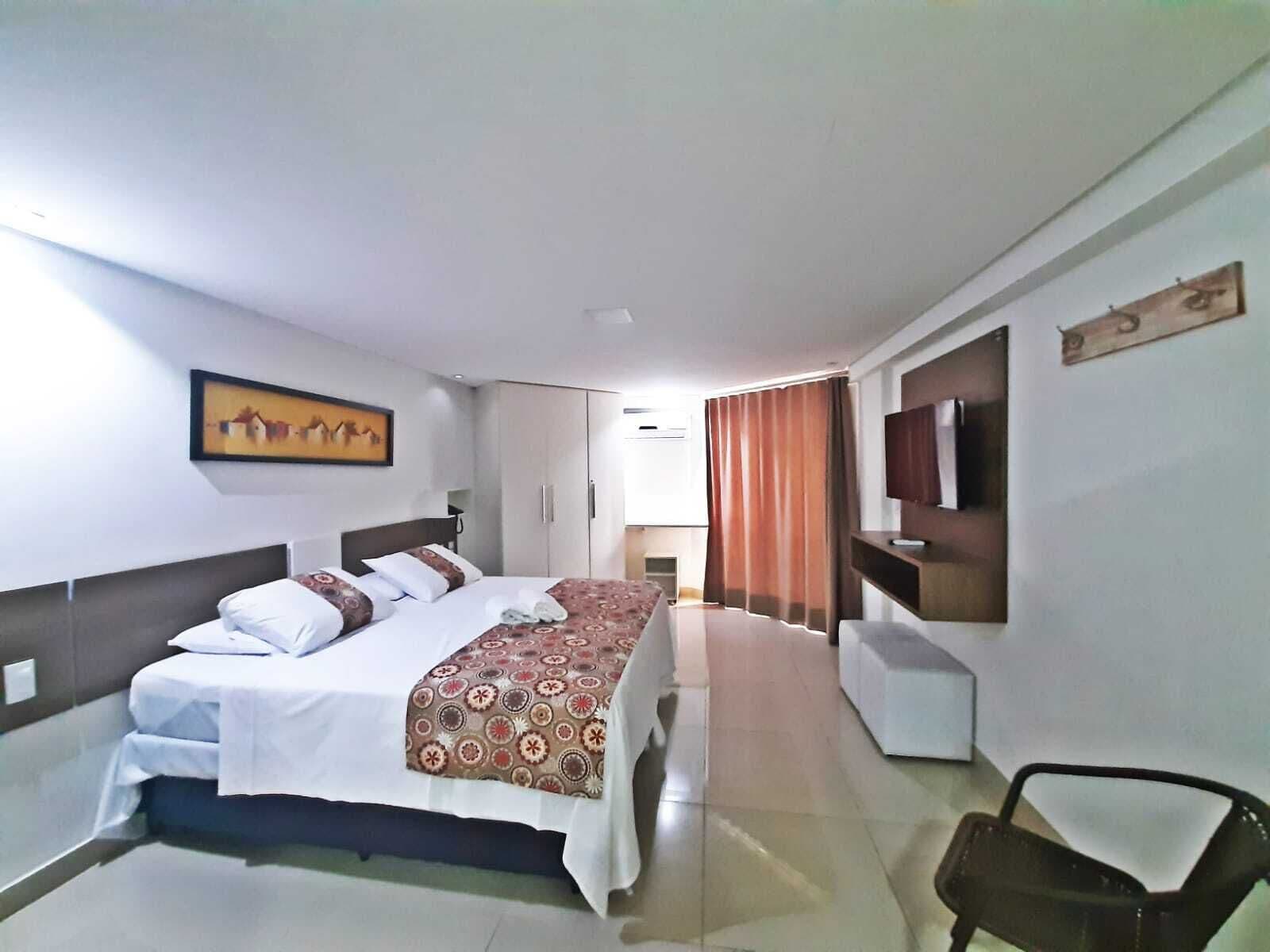 Una habitación de hotel con cama, una silla, televisor y un cuadro en la pared.