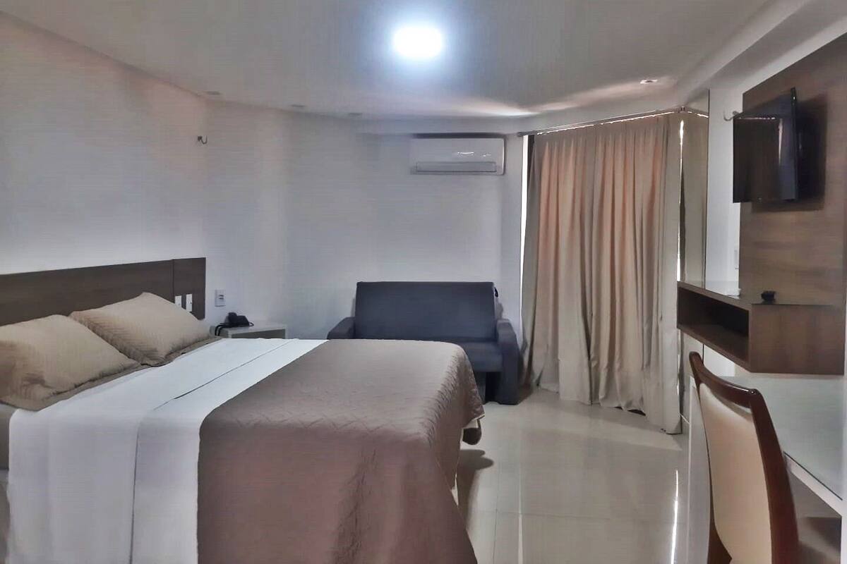 Una habitación de hotel con cama, escritorio, silla, televisor y aire acondicionado.