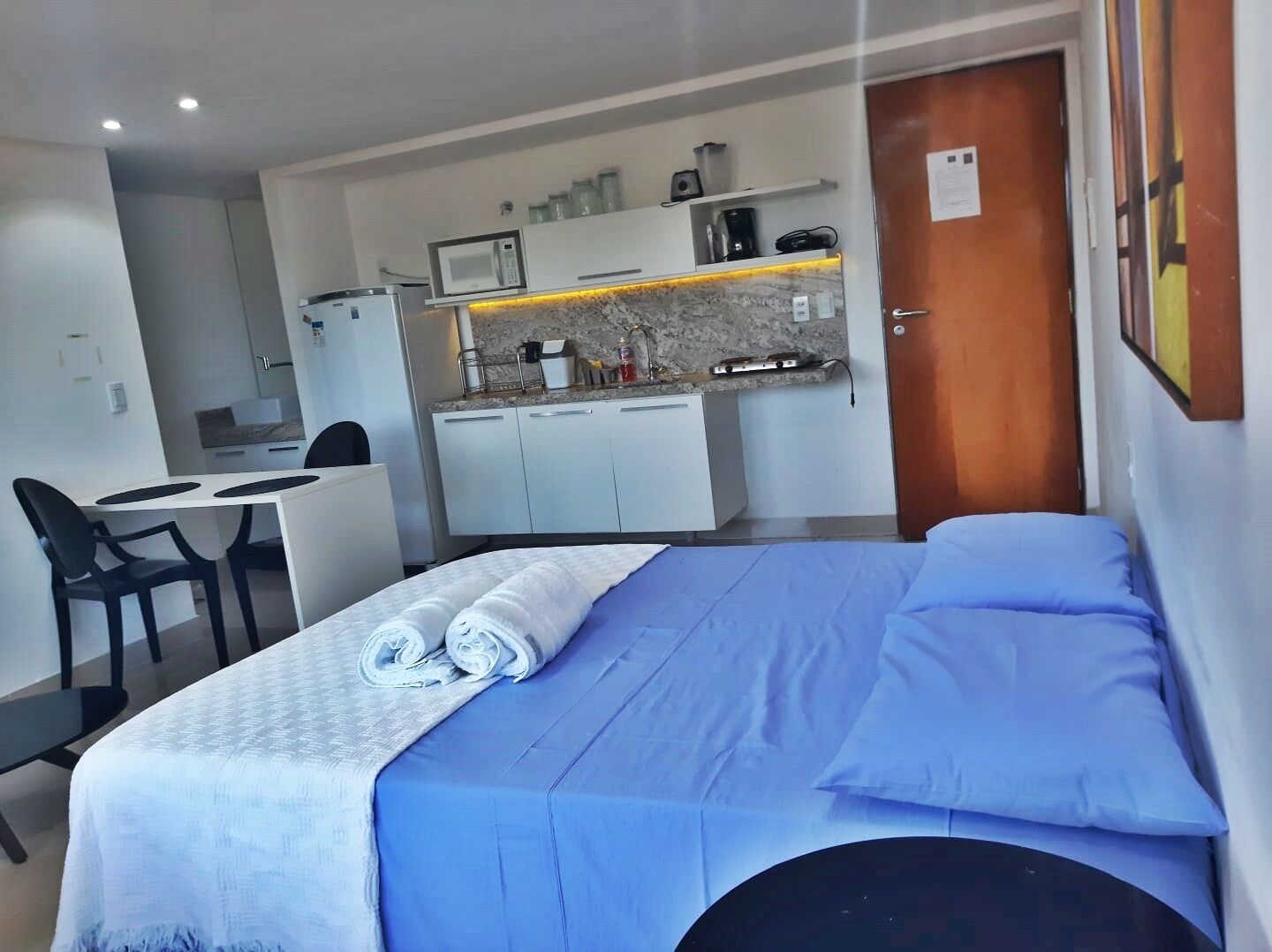 Ein kleines Hotelzimmer mit Bett, Schreibtisch und einer Küchenzeile.