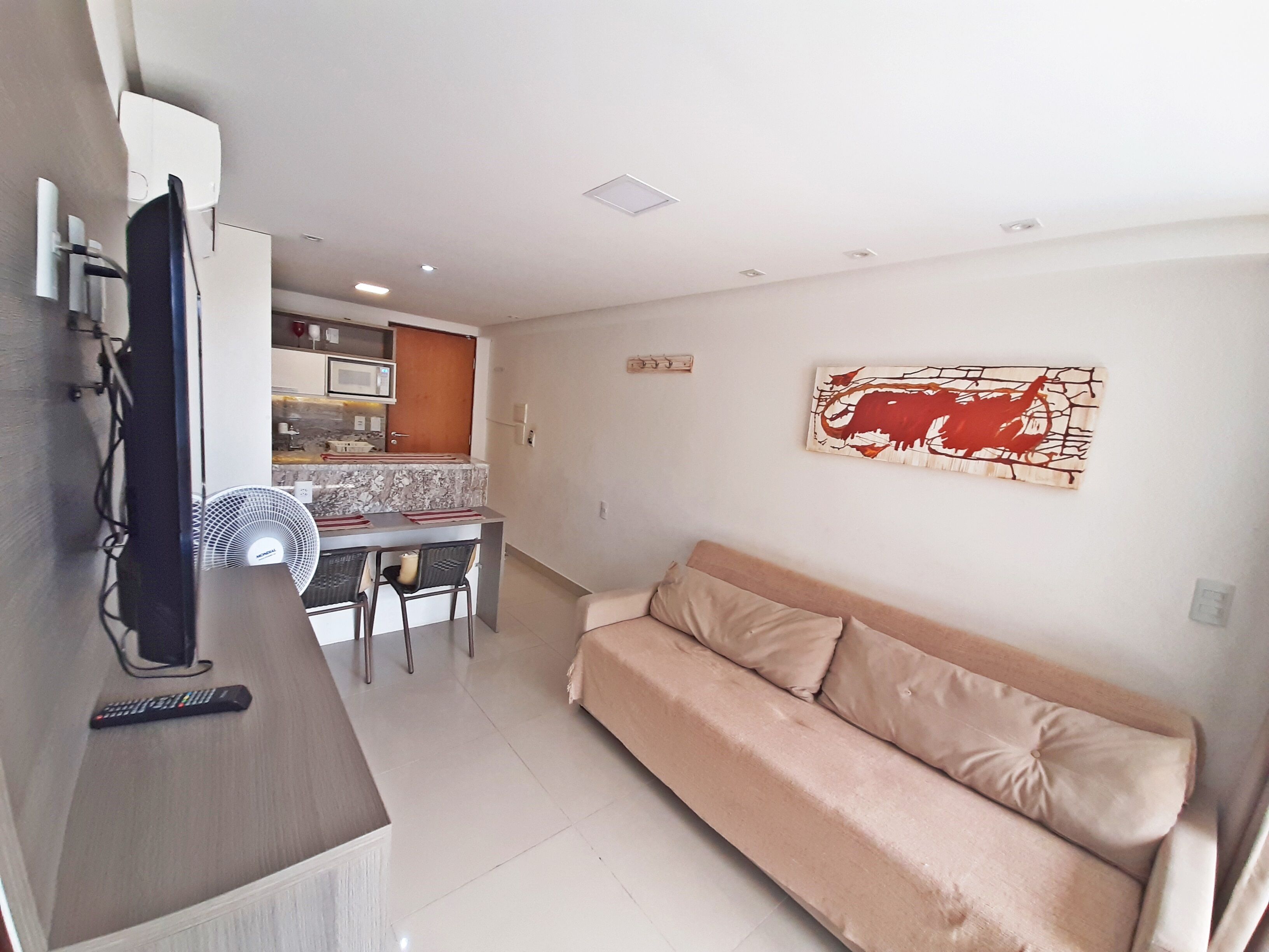 A living room with a beige sofa, a TV, and a dining area with a table and chairs.