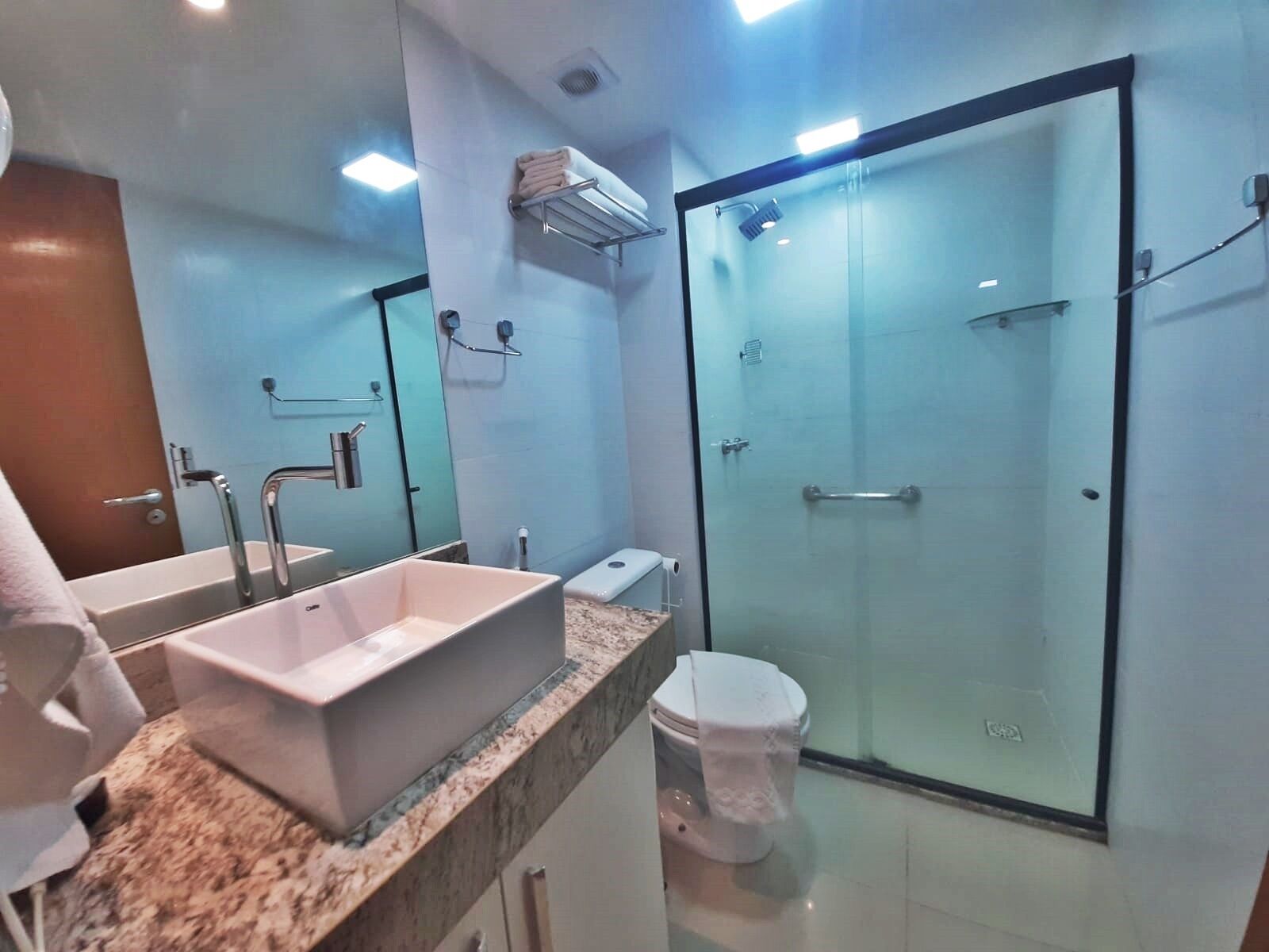 Un bany modern amb una cabina de dutxa de vidre gran, un lavabo blanc i un vàter.