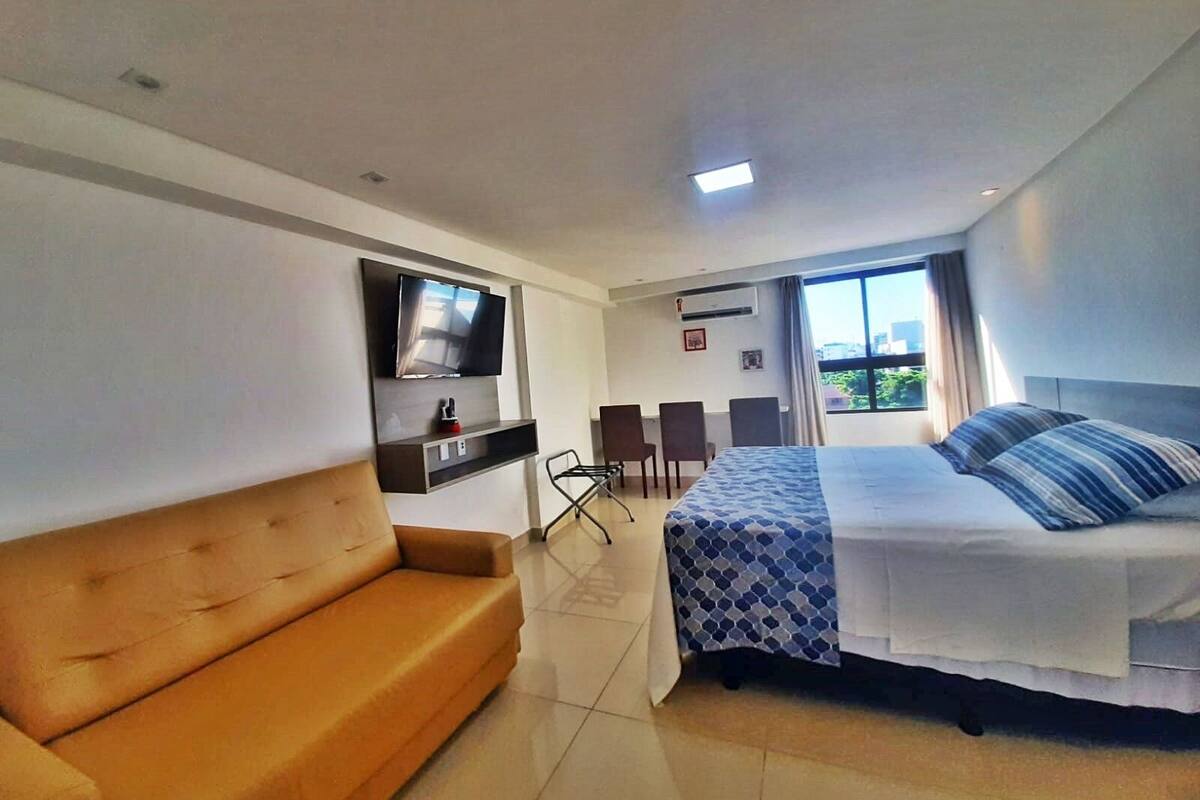 Una habitación de hotel con cama, sofá, televisión, escritorio y ventana con vistas.
