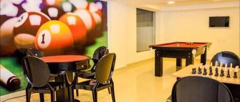 A billiards room with a pool table, a foosball table, and a large mural of billiard balls.