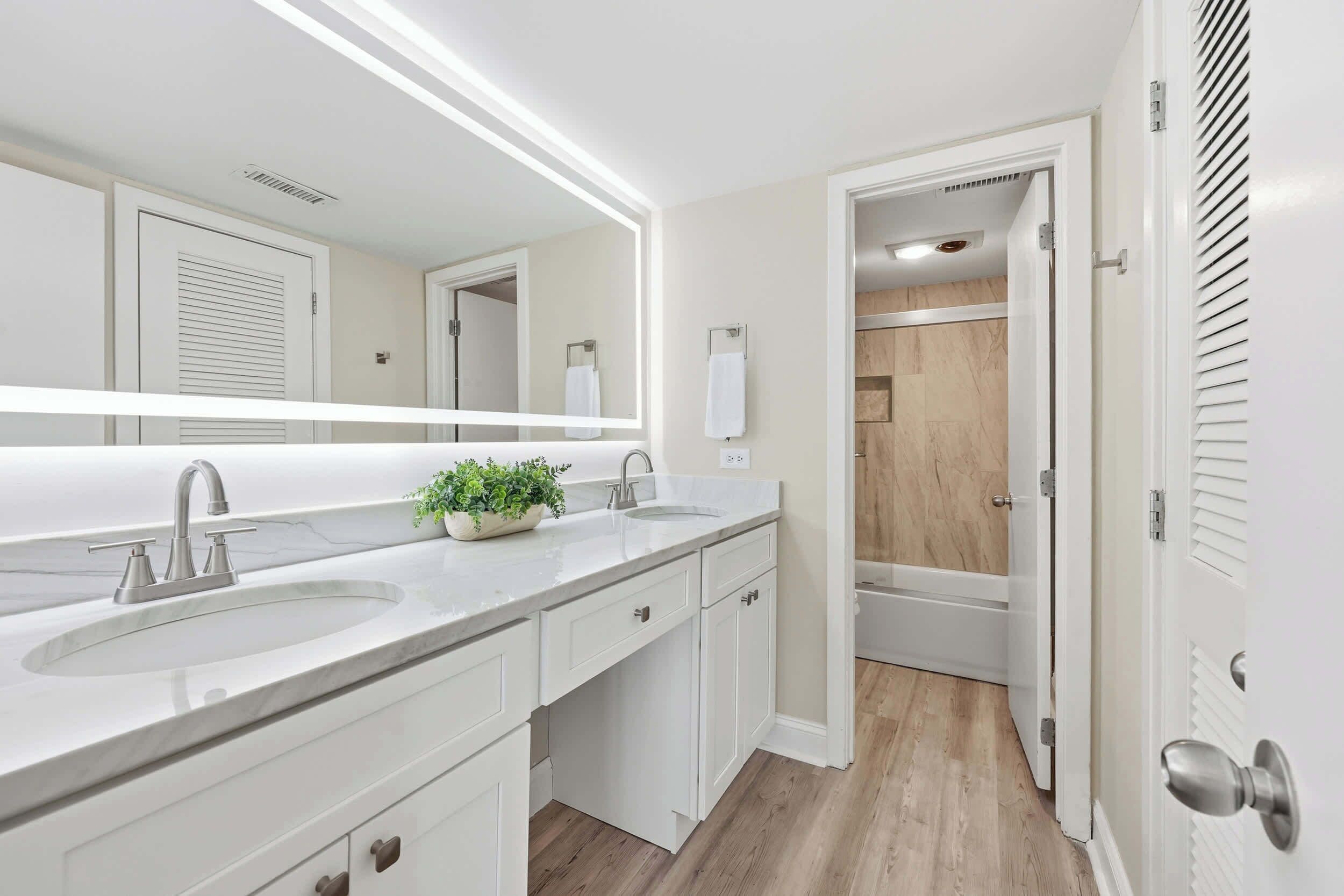 A modern bathroom with a large mirror, two sinks, and a shower area.
