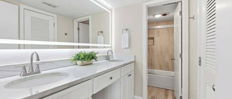 A modern bathroom with a large mirror, two sinks, and a shower area.