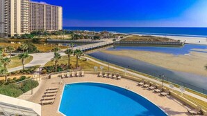 Ein Hotelpool mit Liegestühlen, Blick auf den Strand und einem Hochhaus im Hintergrund.