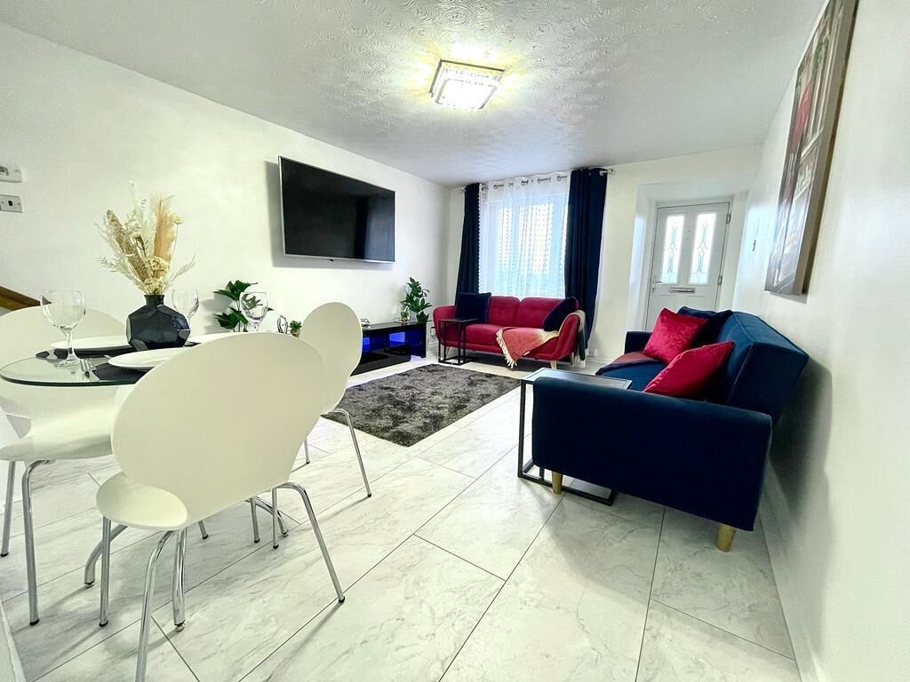 A modern living room with a dining area, a flat-screen TV mounted on the wall, and a red and blue sofa set.