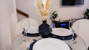 Une table à manger dressée avec de l’argenterie blanche, de la verrerie transparente et un vase décoratif contenant des fleurs séchées.