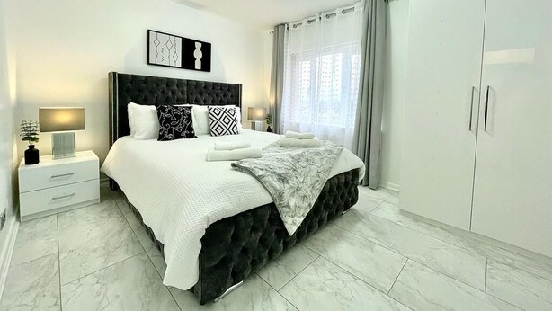 Une chambre moderne avec un grand lit, une table de chevet, une armoire et une fenêtre avec des rideaux.