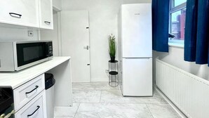 Une cuisine de taille réduite avec des meubles blancs, un four à micro-ondes, un réfrigérateur et une plante en pot.