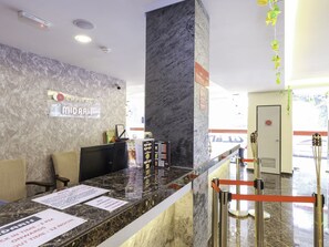 Bancada de recepção de hotel com detalhes em mármore, um computador e folhetos informativos.