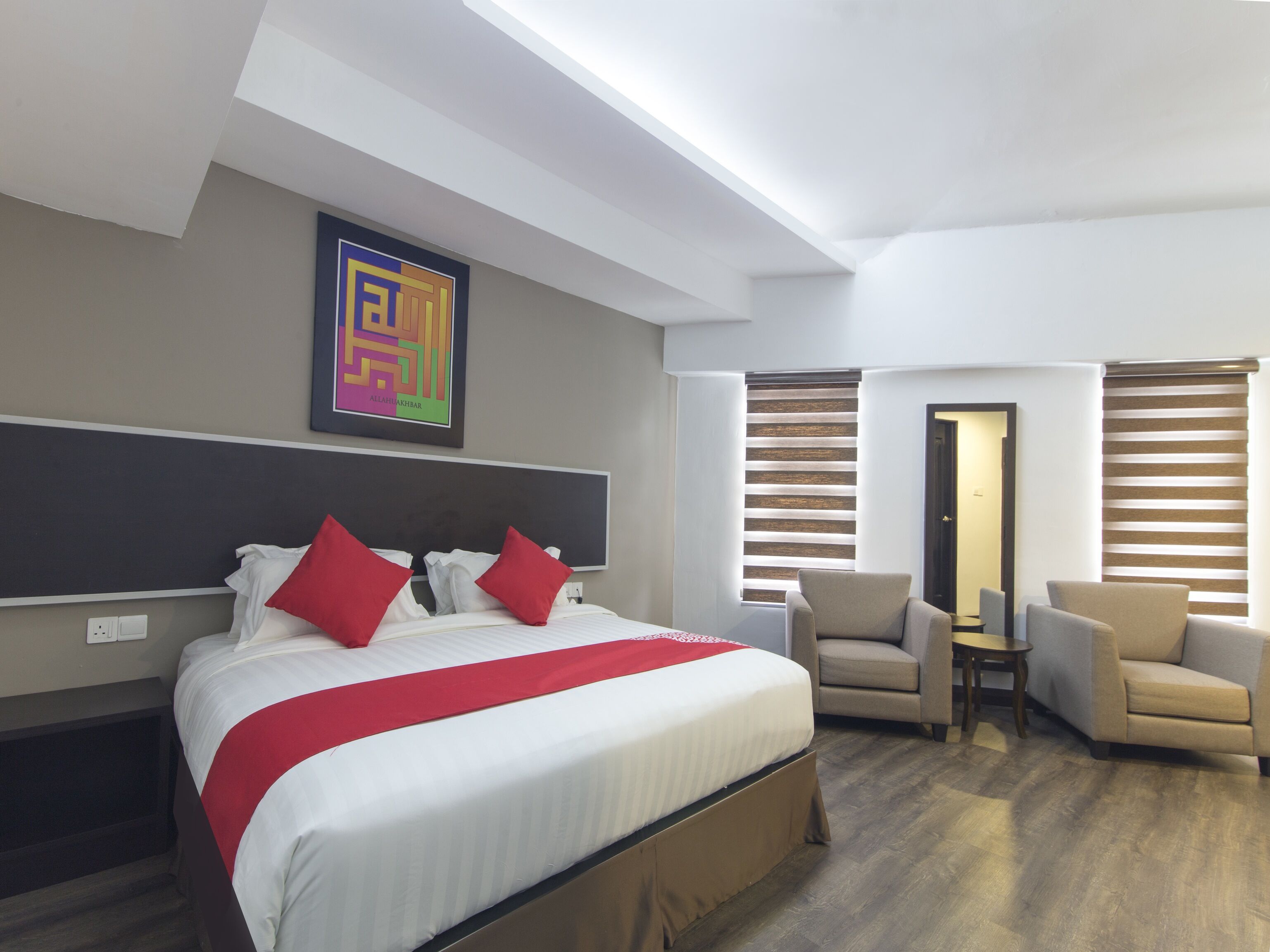A modern hotel room with a large bed, a desk, and two armchairs.