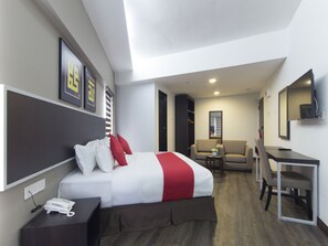 Quarto de hotel com uma cama, escrivaninha, cadeira, sofá e televisão.