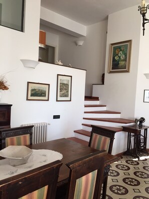 A dining area with a wooden table and chairs, a radiator, and a staircase leading to an upper level.