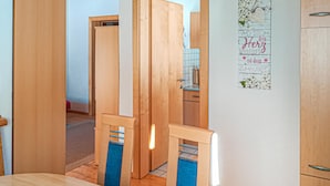 A room with a wooden dining table, chairs, a kitchen area, and a wall with a decorative poster.