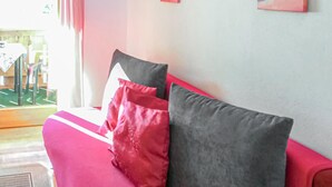 A red sofa with two pillows, a window with curtains, and a view of an outdoor area with a table and chairs.