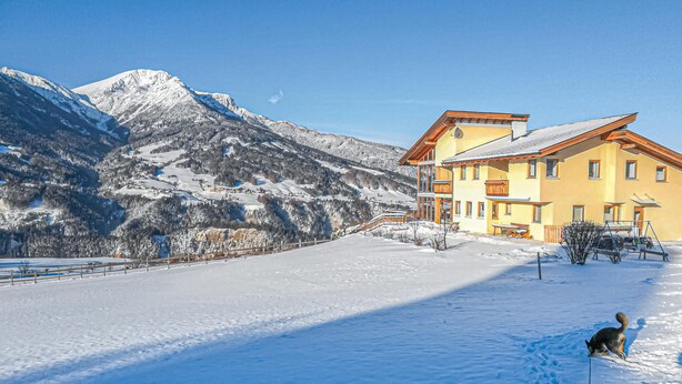A snow-covered mountain landscape with a yellow building featuring balconies and a wooden deck.