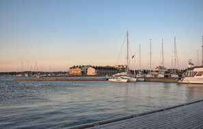 Uma marina com vários veleiros atracados, um cais de madeira e edifícios ao fundo.