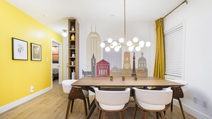 A dining area with a wooden table, white chairs, and a cityscape mural on the wall. - Mid Century Modern townhome in Historical Downtown Noblesville (Noblesville)