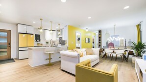 A modern kitchen with white cabinets, a yellow accent wall, and a cityscape view through the window. - Mid Century Modern townhome in Historical Downtown Noblesville (Noblesville)