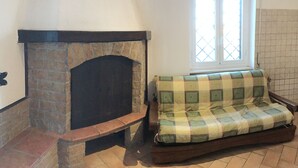 A living room with a stone fireplace, a window with a grid pattern, and a checkered sofa. - The Attichetto (Ciampino)