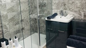 A modern bathroom with a glass-enclosed shower, a white sink, and a dark vanity.