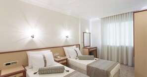 A hotel room with two beds, a bedside table with a lamp, a mirror, and a window with curtains. - Villa Sunflower Hotel (Alanya)