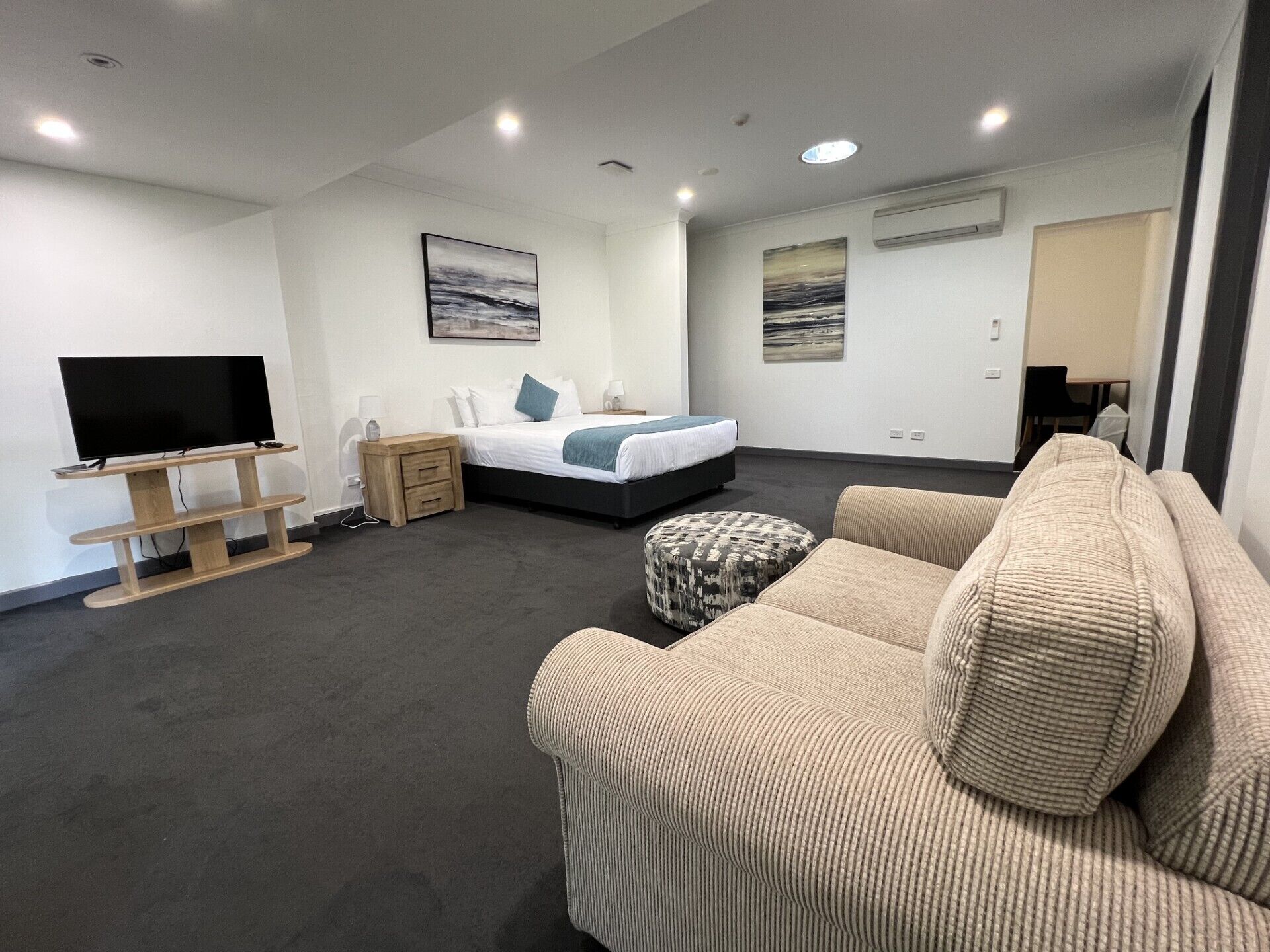 A modern hotel room with a bed, a TV, a sofa, and artwork on the walls.