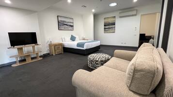 A modern hotel room with a bed, a TV, a sofa, and artwork on the walls.