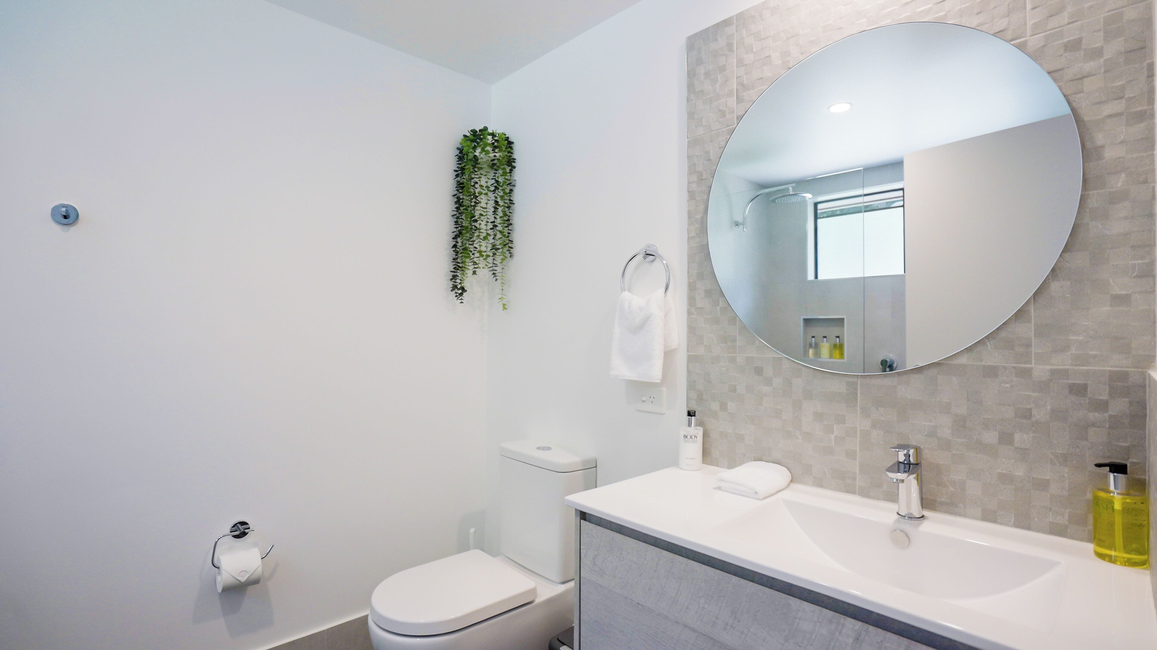 Un baño moderno con inodoro, lavamanos y espejo.