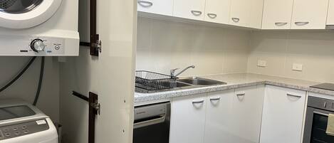 A kitchen with white cabinets, a stainless steel sink, a dishwasher, and a washing machine.