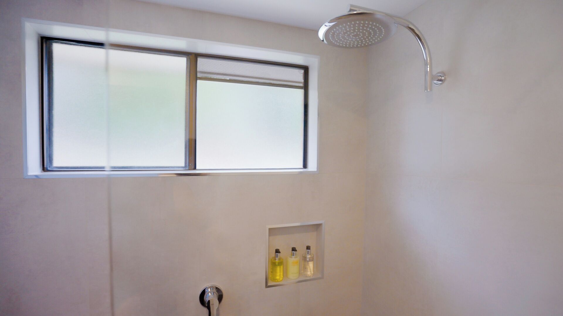 Una ducha con ventana, un perchero y un estante con botellas.