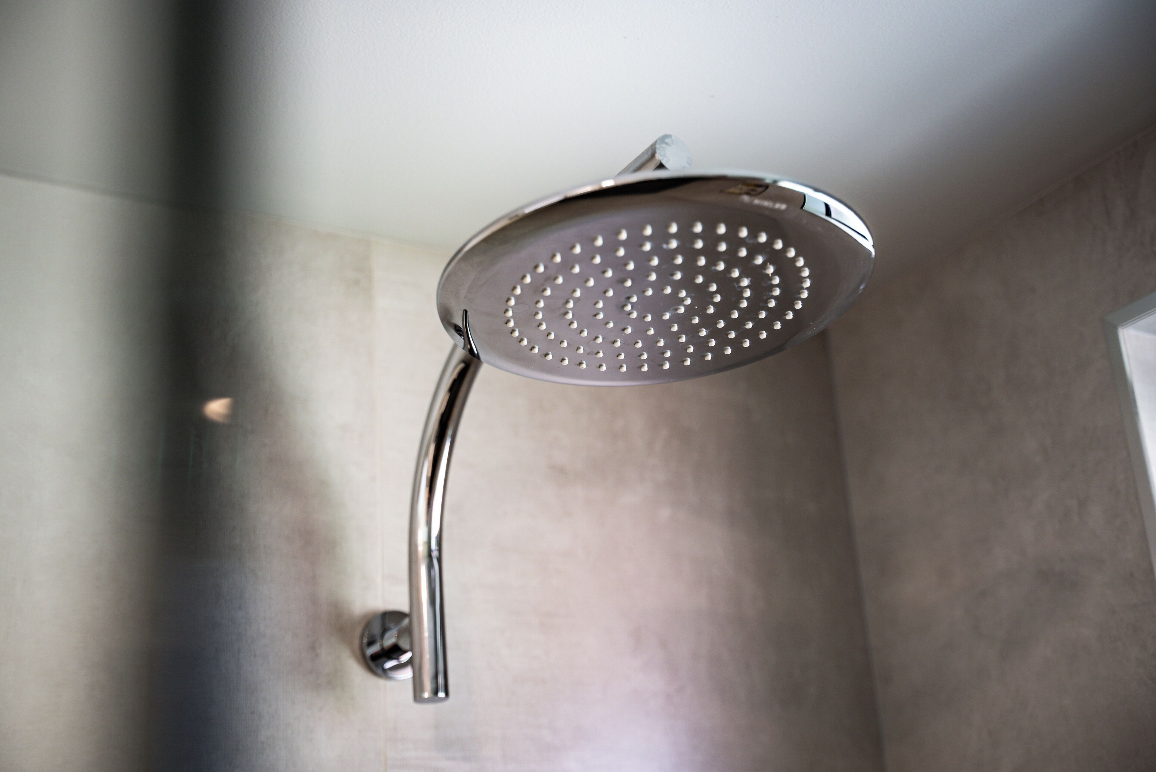 Ein moderner Duschkopf mit gebogener Form, an einer Wand mit metallischer Oberfläche angebracht.