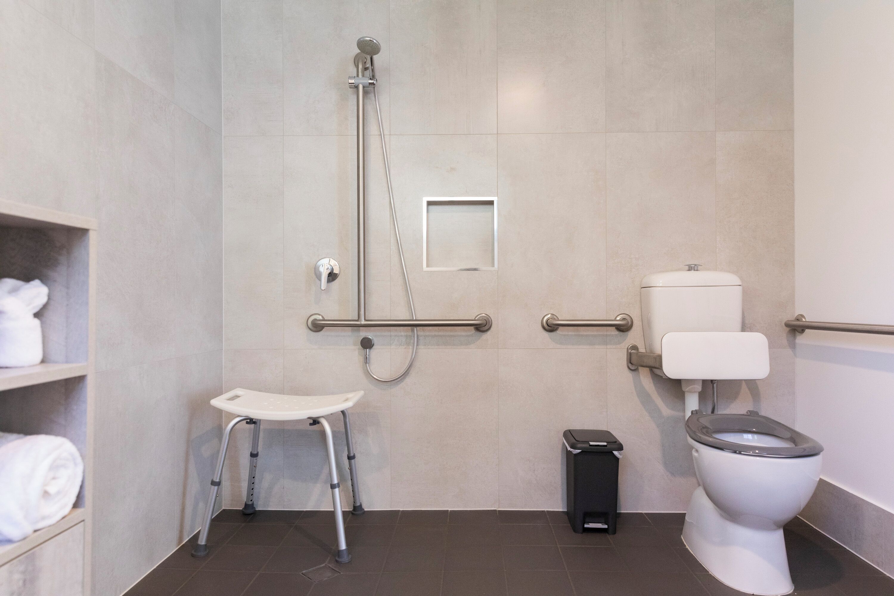 A modern bathroom with a shower, toilet, and a wheelchair-accessible bench.