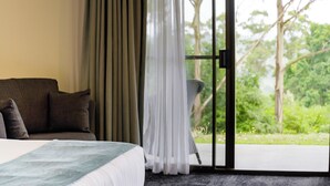 Ein Schlafzimmer mit Bett, Stuhl und Blick auf Grün durch eine Glastür.
