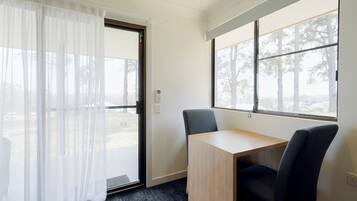 Una habitación con escritorio, dos sillas, una puerta con cortina y ventanas con vista a árboles.