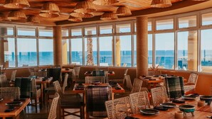 A restaurant with wicker furniture, large windows, and a view of the ocean.