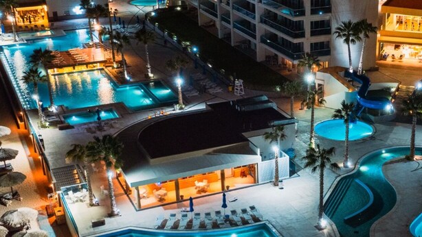 A resort pool area with multiple swimming pools, lounge chairs, and palm trees.