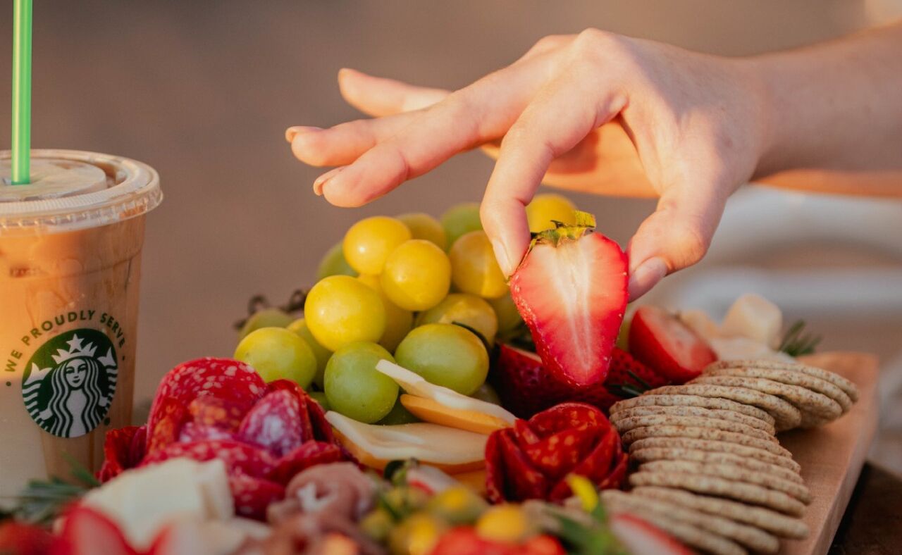 A tray of assorted fruits and snacks, including grapes, strawberries, and crackers, with a Starbucks cup in the background.