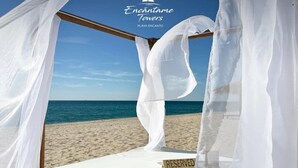 A bed with a 'RESERVED' sign, white curtains, and a wooden frame against a beach backdrop.