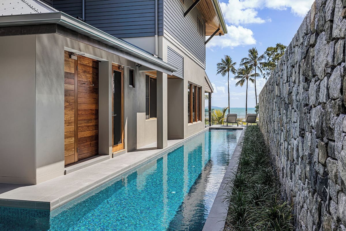 A modern building with a swimming pool, stone wall, and palm trees.