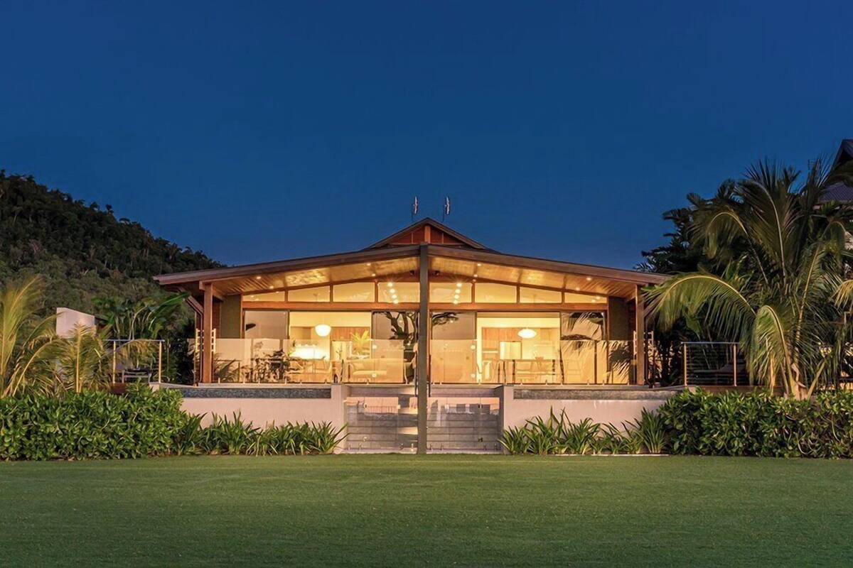 A modern house with a glass facade, surrounded by lush greenery and a well-maintained lawn.