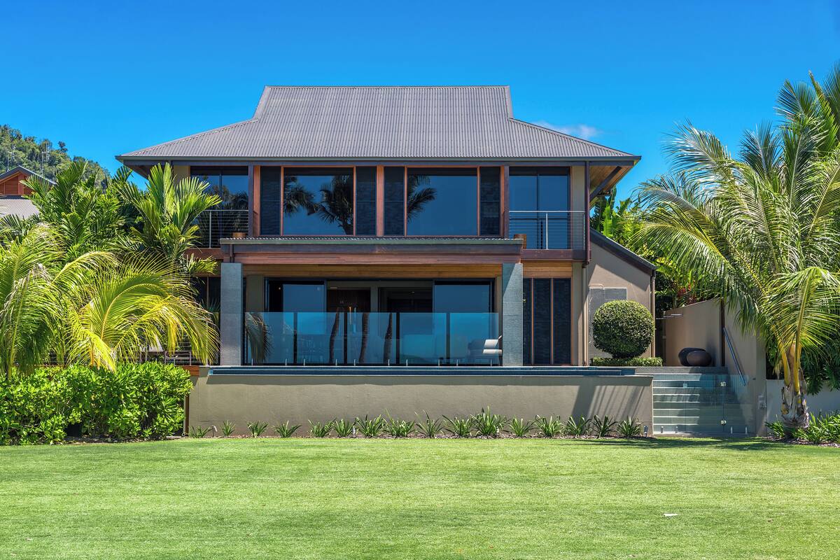 A modern two-story house with a flat roof, large windows, and a well-maintained lawn.