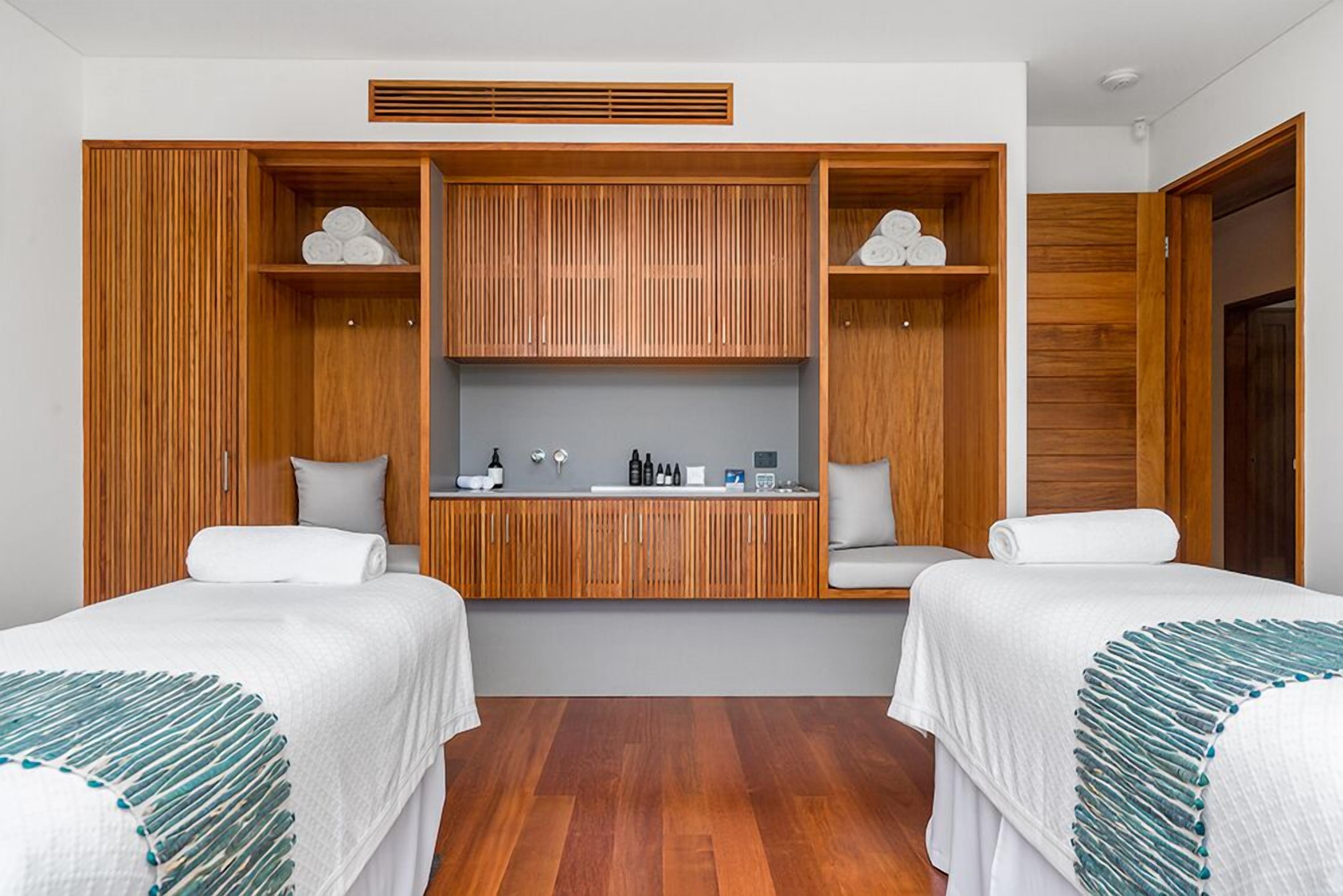 Una habitación de hotel con dos camas, un armario de madera, una pequeña kitchenette y un banco empotrado.